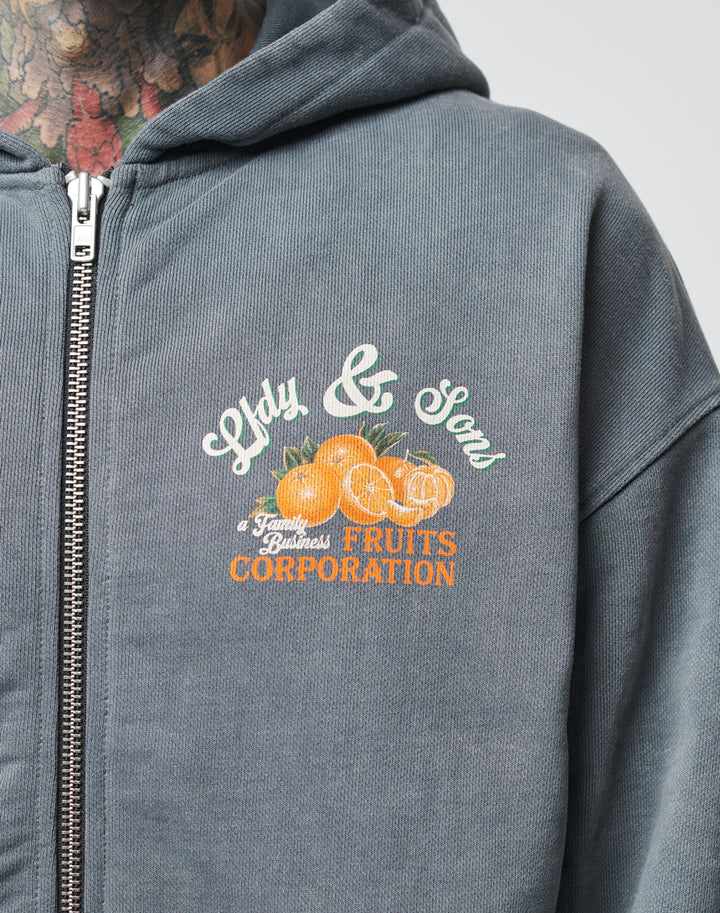 A gray zip-up hoodie by LIVE FAST DIE YOUNG, named Lfdy & Sons Hooded Zip, features a colorful orange graphic and the text Lily & Sons, A Family Business, Fruits Corporation, with a vintage effect and oversize fit; wearer has neck tattoos.