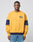 A man stands against a light gray background wearing the LFDY® Sweater by LIVE FAST DIE YOUNG—a yellow sweatshirt with navy blue sleeve stripes and a small circular logo on the left chest—paired with light blue jeans.