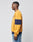 A man in profile stands against a plain background, wearing the LFDY® Sweater by LIVE FAST DIE YOUNG—an oversized yellow sweatshirt with a wide navy blue sleeve stripe made from soft Baumwolle—paired with blue jeans.