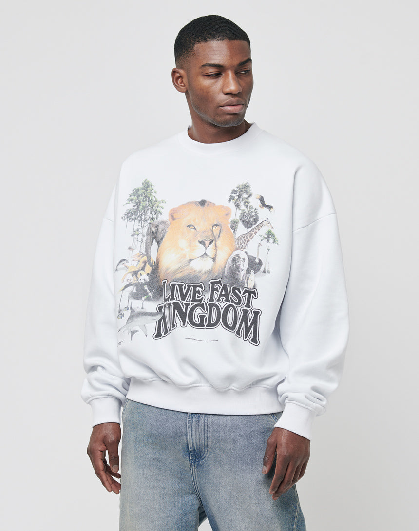 A man stands against a plain light background wearing the LFDY Vintage Lion Sweater, featuring a bold lion frontprint and "Live Fast Kingdom" slogan, paired with light blue jeans.