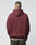 A person faces away from the camera in a LIVE FAST DIE YOUNG Import & Export Hooded sweatshirt, maroon and oversized with a subtle vintage effect, layered over a white shirt and dark pants against a plain light gray background.