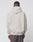 Someone stands with their back to the camera, wearing the LIVE FAST DIE YOUNG Survival Hooded light beige oversize-fit cotton sweatshirt and dark pants with a red stripe, set against a plain light background.