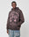 A man wears the LIVE FAST DIE YOUNG Wisdom Hooded—an Oversize Fit dark hoodie with pink parachute graphics and vintage Effekt, made from soft Baumwolle—as he stands against a plain gray background, looking to the side with one hand at his waist.
