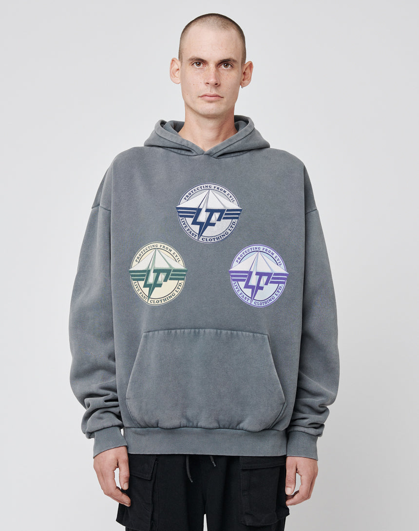 A person wears the Triple LF Hooded by LIVE FAST DIE YOUNG—a loose, gray hoodie with a vintage effect and three bold, colorful circular logo frontprints (stylized text and wings)—standing against a plain light background.