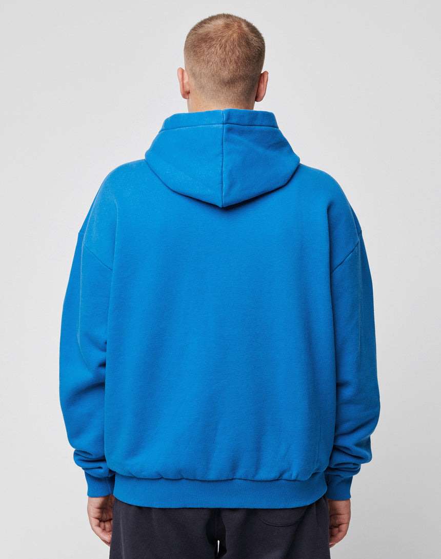 A person with short hair stands with their back to the camera, wearing a bright blue Basic Chest Hooded by LIVE FAST DIE YOUNG and black pants against a plain light gray background.