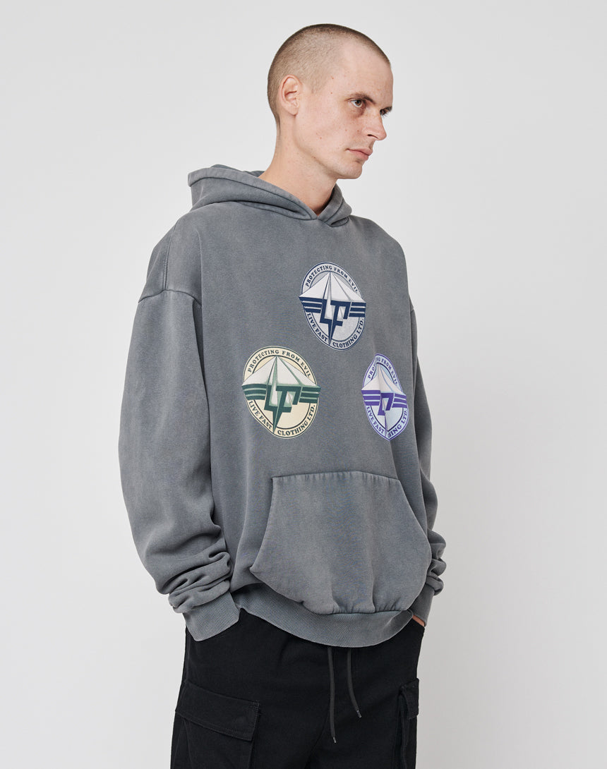 A person with short hair wears the LIVE FAST DIE YOUNG Triple LF Hooded, a loose gray hoodie with three colorful circular logos on the front, paired with black cargo pants, standing against a plain light background.