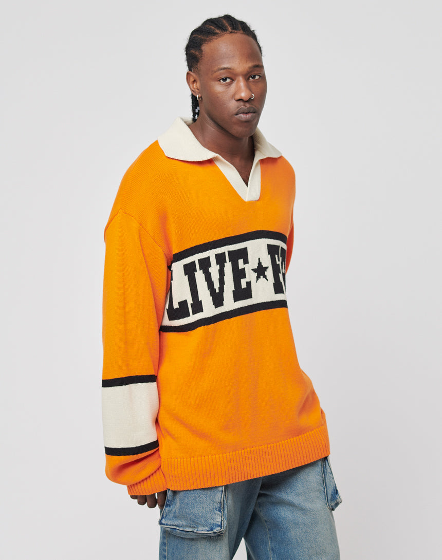 A person wearing an orange and white LFDY Knit Polo by LIVE FAST DIE YOUNG, paired with blue jeans, stands against a plain light background.