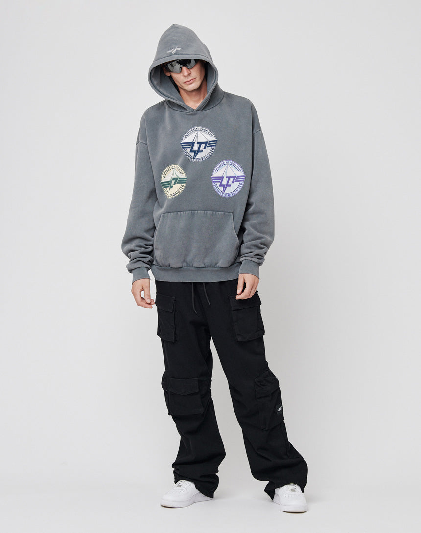 A person in LIVE FAST DIE YOUNG’s Triple LF Hooded—an oversized gray hoodie with multicolored circular logos and a front print—pairs it with black cargo pants, white sneakers, and sunglasses, standing against a plain white background.