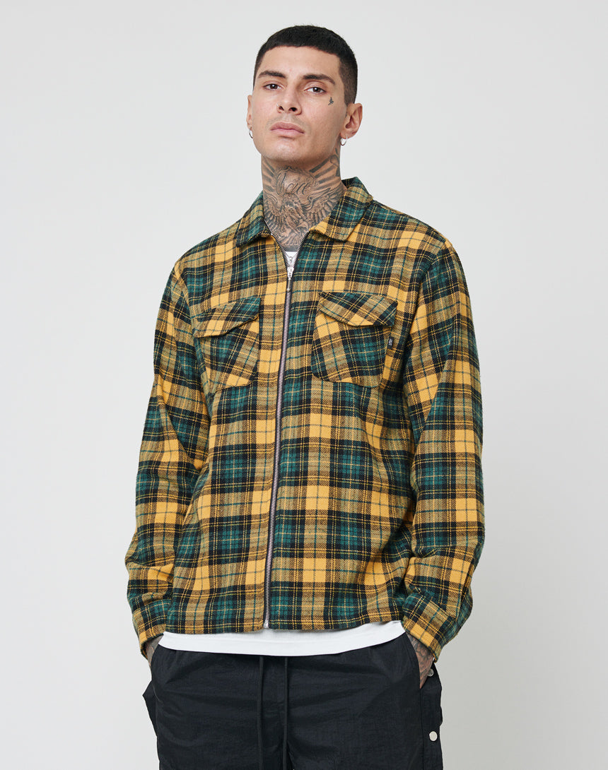 A person with short dark hair and neck tattoos wears an oversize yellow and green LFDY Zip Flannel over a white tee, paired with black pants, standing against a plain light background.