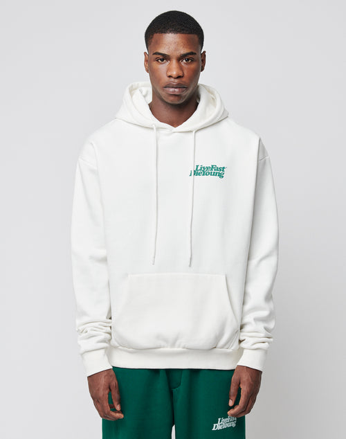 A man wearing a LIVE FAST DIE YOUNG Basic Chest Hooded hoodie with Live Fast Die Young in green on the chest and matching green shorts, stands against a plain light background.