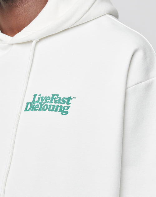 A person wears an oversized white Basic Chest Hooded sweatshirt by LIVE FAST DIE YOUNG, featuring green LiveFast DieYoung text on the chest. Only part of their face and upper body is visible.