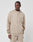 A person wears the LIVE FAST DIE YOUNG Knit Hooded Zip hoodie in beige with a chest logo patch and matching pants, standing against a white background, looking to the side with one hand in their pocket.