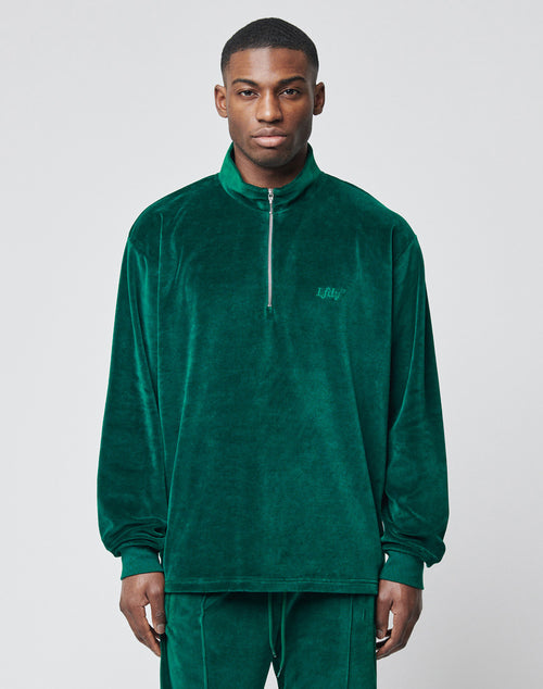 A man faces forward in a green LIVE FAST DIE YOUNG Velvet Halfzip pullover with Metallreißverschluss half-zip and matching oversize-fit pants, set against a plain light gray background.