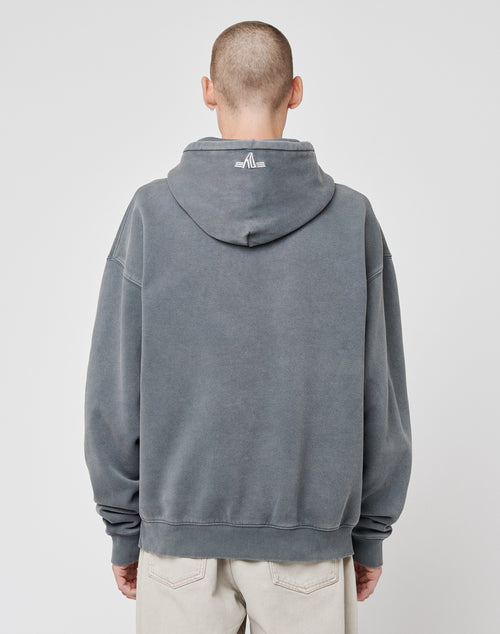 A person with a buzz-cut is wearing the LIVE FAST DIE YOUNG Beginning Hooded in an oversize fit, featuring a small white graphic on the upper back, paired with light pants against a plain white background.