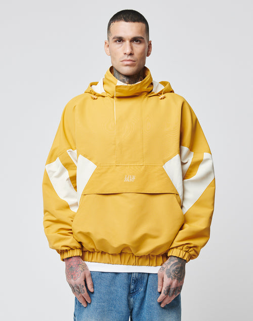 A man with short hair and hand tattoos wears the LIVE FAST DIE YOUNG Half Zip Hooded Jacket in mustard yellow and white, featuring a front pocket and drawstring hood, standing against a plain light gray background.