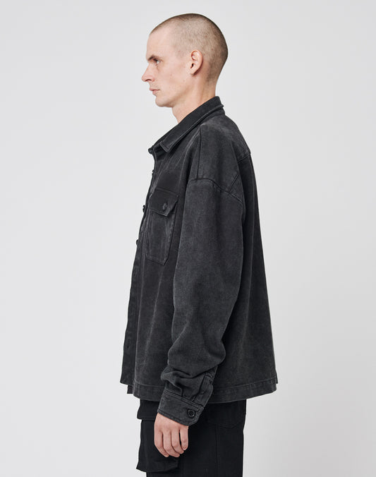 A person with a shaved head stands in profile facing left, wearing the LIVE FAST DIE YOUNG Vintage Dyed Flannel, an oversized black button-up jacket with chest pockets, and black pants against a plain white background.