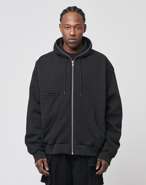 A person faces forward in a black Waffle Hooded Zip by LIVE FAST DIE YOUNG, featuring an oversize fit, chest pocket, and subtle Logo-Stick, layered over a black shirt against a light plain background.