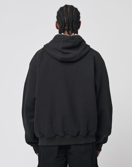 A person with braided hair is seen from behind wearing the LIVE FAST DIE YOUNG Waffle Hooded Zip and black pants, set against a plain light background.