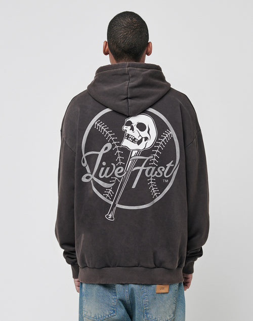 A person wears the LIVE FAST DIE YOUNG Live Fast Skull Hooded, an oversized hoodie with bold front and back prints—a skull on a baseball bat, crossed baseballs, and Live Fast—paired with light blue jeans, facing away.