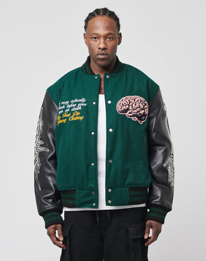A person stands facing forward wearing the Life College Jacket by LIVE FAST DIE YOUNG—green with leather sleeves, logo snap buttons, embroidered brain and text on the chest, and white graphics on the sleeves—over a white shirt and black pants.