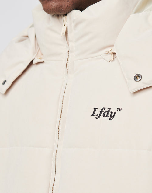 Close-up of a person wearing the LFDY Basic Winter Jacket in light beige. This oversized, padded winter jacket features a high collar, snap buttons, wind- and weatherproof design, and LFDY embroidery on the chest.