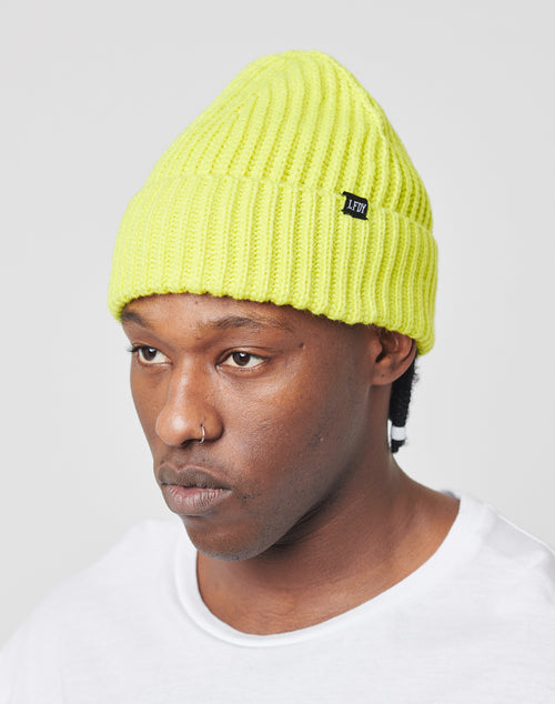 A person wearing a bright yellow LFDY Rib Knit Beanie with a small black tag and a plain white shirt, looking slightly to the side against a neutral background.