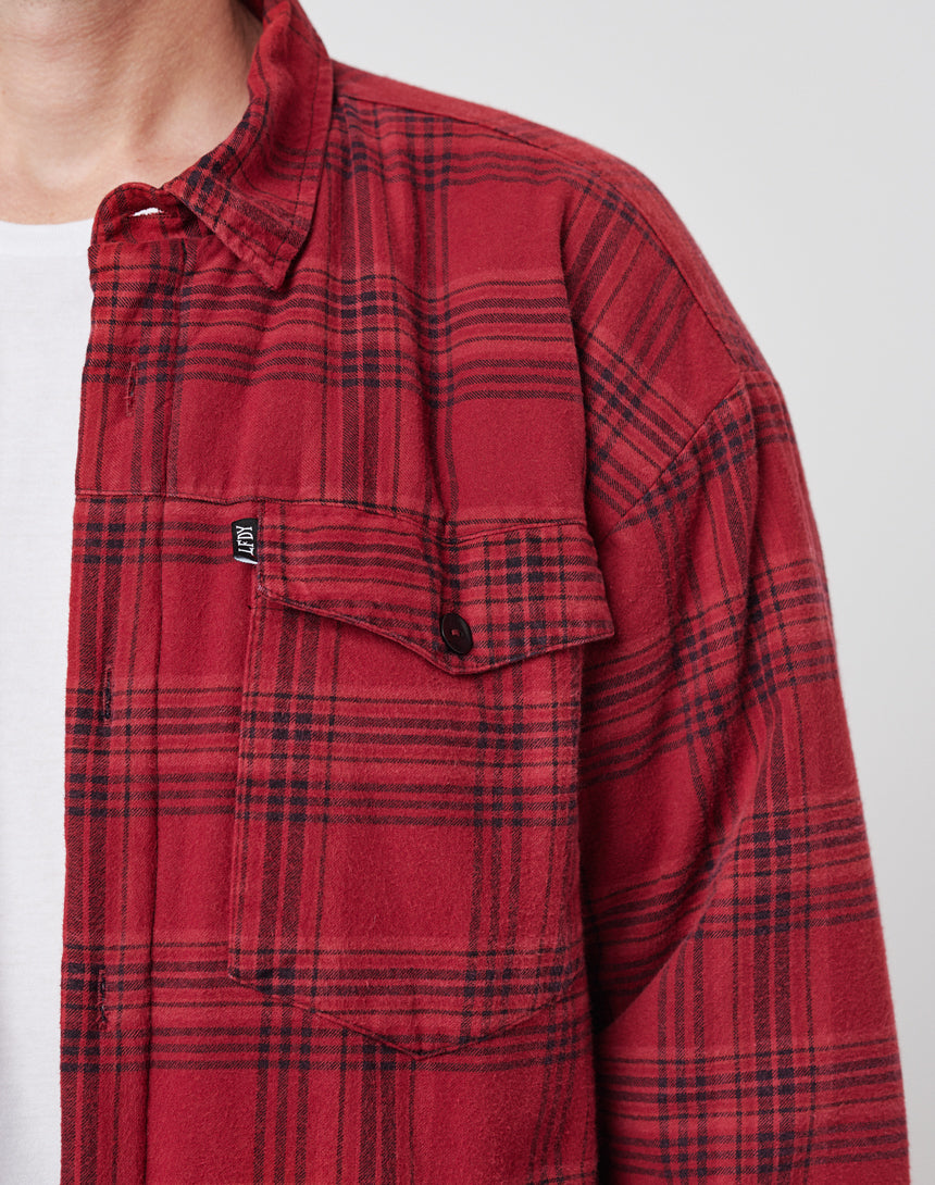 A person wears a LIVE FAST DIE YOUNG Padded Flannel Jacket with red and black plaid, zweiteiliger Hemdkragen, and oversize fit over a white t-shirt. Only the upper torso and part of the face are visible against a plain, light background.