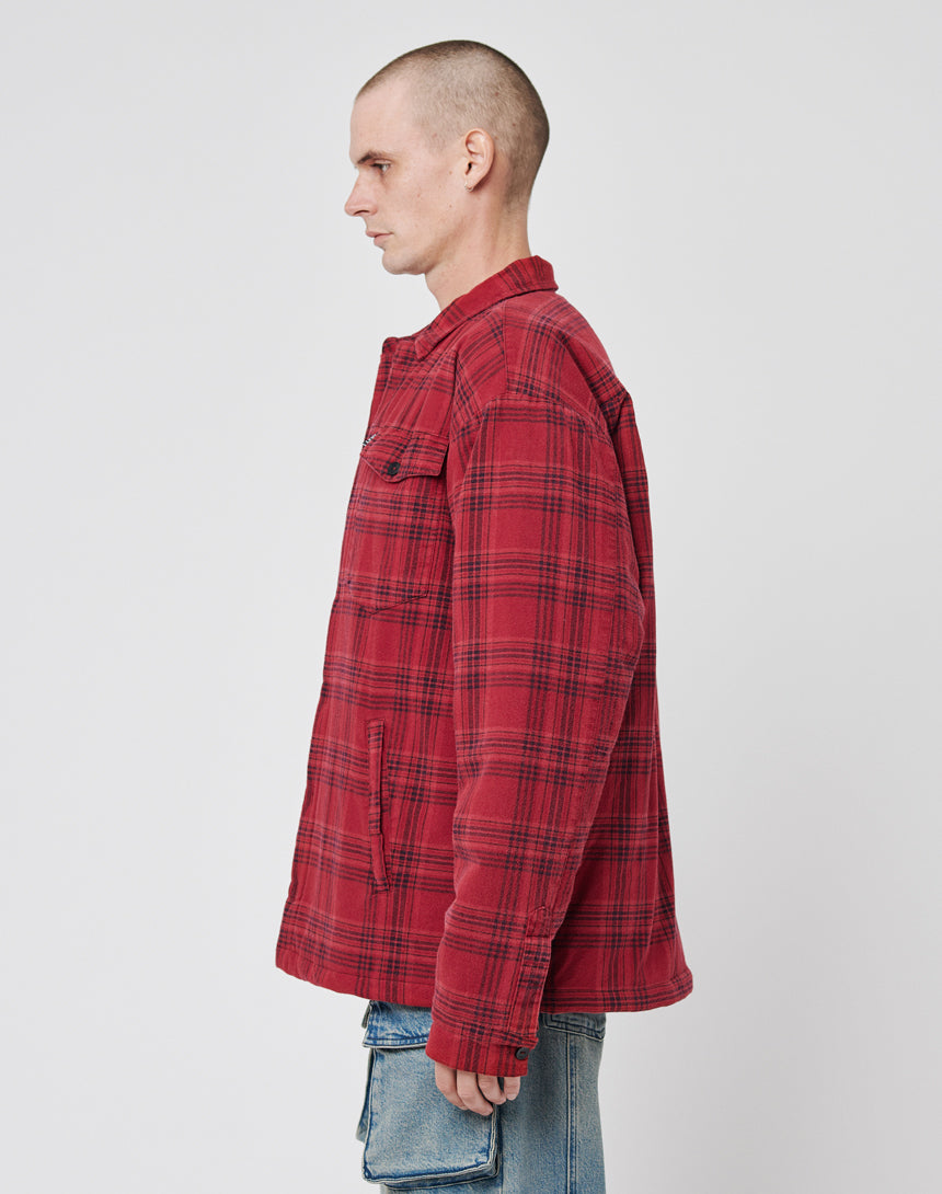 A person with a shaved head wearing the LIVE FAST DIE YOUNG Padded Flannel Jacket and blue jeans stands in profile facing left against a plain white background.