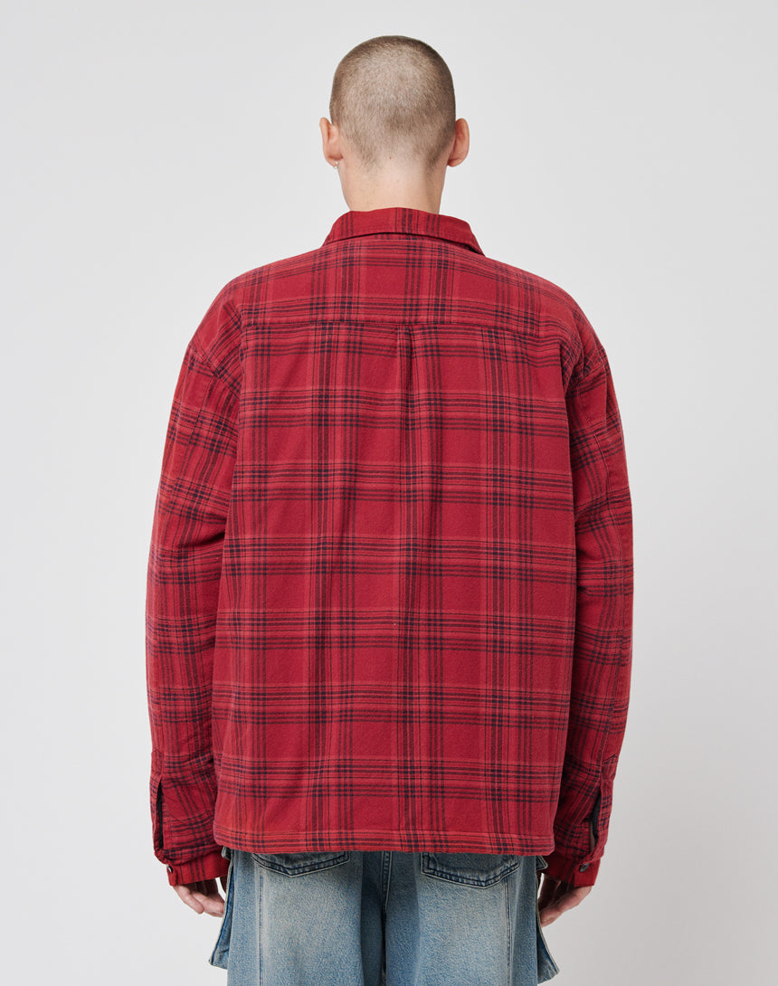 A person with a shaved head wears the LIVE FAST DIE YOUNG Padded Flannel Jacket with Zweiteiliger Hemdkragen and light blue jeans, standing back to camera against a plain light background for a subtle vintage effect.
