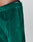 Close-up of a person wearing LIVE FAST DIE YOUNG Velvet Tracksuit Pants in green velour with an elastic waistband, side pocket, and logo embroidery on the waistband and leg. Made from premium cotton-polyester blend.