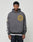 A young man wears the LIVE FAST DIE YOUNG LFDY Department Hooded in dark gray, featuring a yellow circular front print, a sleeve patch, and white text down the right sleeve, standing against a plain light background.