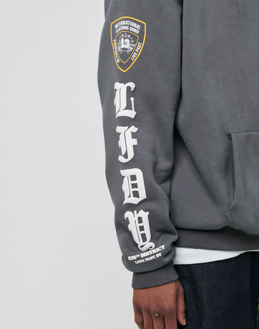 A person wears the oversize fit gray LFDY Department Hooded by LIVE FAST DIE YOUNG, featuring a yellow shield patch on the sleeve, large white Gothic Siebdruck LFDY lettering down the forearm, and smaller white text at the wrist.