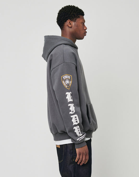 A young man in profile wears the LIVE FAST DIE YOUNG LFDY Department Hooded in gray, featuring an FDNY patch on the arm, bold white LFDNY sleeve lettering, a vintage-effect Siebdruck frontprint, and dark jeans against a light backdrop.