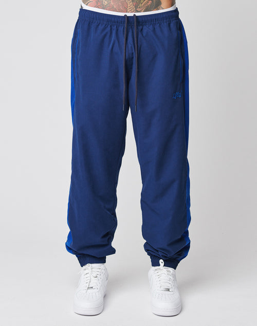 A person is wearing LFDY Trackpants by LIVE FAST DIE YOUNG—blue jogger pants with elastic waistband and drawstring, regular fit, styled with white sneakers. Photo captures only the lower half against a plain background.