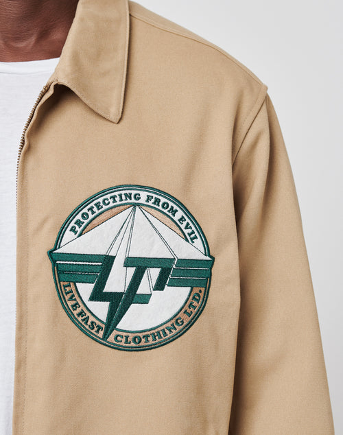 A close-up of the Live Fast Twill Jacket by LIVE FAST DIE YOUNG, featuring a Hemdkragen, large chest patch with “Protecting From Evil” and “Live Fast Clothing Ltd” on a green/white graphic. Regular fit, 100% Baumwolle. White shirt underneath.