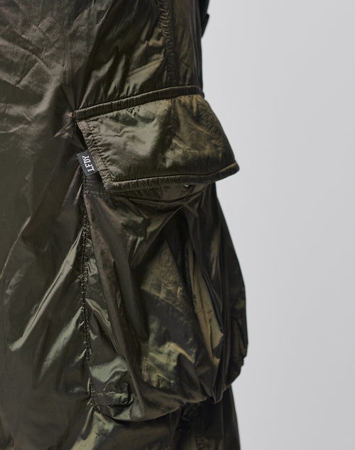 Close-up of the Parachute Cargo by LIVE FAST DIE YOUNG, showing shiny metallic dark green nylon with a large angled cargo-style flap pocket and a small black tag with white text on the seam, set against a plain light background.