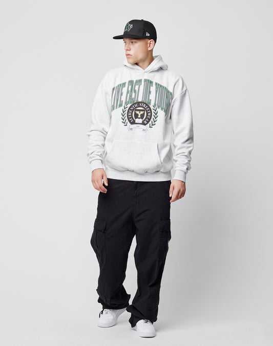 A young man in a black cap, light gray hoodie with a large printed crest, LFDY Wide Summer Cargo pants, and white sneakers stands against a plain white background, looking to his left.