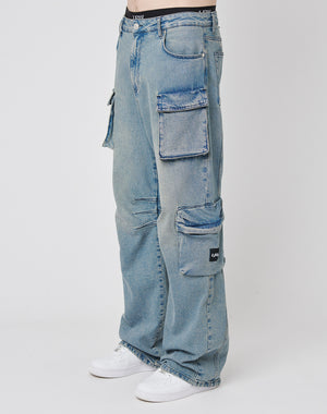 A person wears LIVE FAST DIE YOUNG’s Wide Denim Cargo jeans—loose-fitting, light blue denim with large side pockets—paired with white sneakers for a relaxed streetwear look.