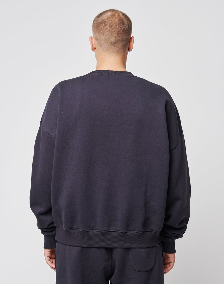 A person with short hair stands with their back to the camera, wearing the LIVE FAST DIE YOUNG Basic Chest Sweater and matching pants in an oversize fit against a plain light background.