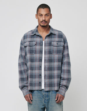 A man stands facing forward in the LIVE FAST DIE YOUNG Loose Flannel Shirt, featuring a gray and pink plaid vintage wash, layered over a white tee and blue jeans against a plain light background.