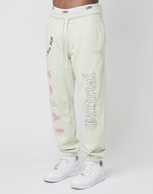 Someone wears the LFDY Official Jogger in light beige—100% Baumwolle sweatpants featuring black and pink graphic text and prints on the front and back, with an elastic waistband and cuffs—paired with white sneakers.