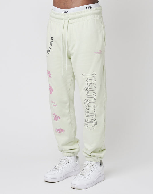 Someone wears the LFDY Official Jogger in light beige—100% Baumwolle sweatpants featuring black and pink graphic text and prints on the front and back, with an elastic waistband and cuffs—paired with white sneakers. | model