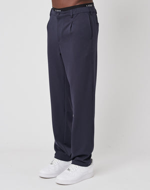 A person models LIVE FAST DIE YOUNG Regular Casual Pants in dark navy blue with an elastic waistband and white sneakers, standing against a plain white background. Only the lower body is shown.