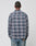 A person stands facing away, wearing the LIVE FAST DIE YOUNG Loose Flannel Shirt in blue, gray, and purple plaid (100% Baumwolle), paired with light blue jeans against a plain light background.