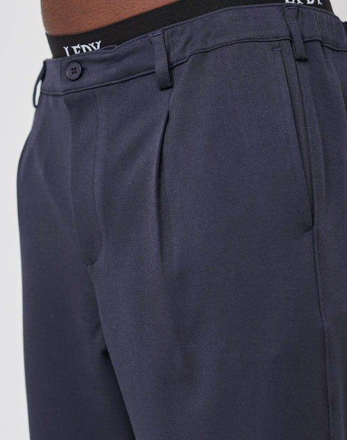 Close-up of a person wearing LIVE FAST DIE YOUNG Regular Casual Pants in dark navy with an elastic waistband, featuring black band with white logo details. Focus is on the fabric texture and regular fit.