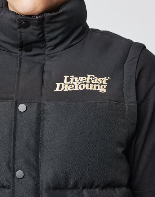 Close-up of a person wearing the LIVE FAST DIE YOUNG Basic Vest with beige Live Fast Die Young embroidery on the chest. Only the lower face, neck, and upper torso are visible. The sleek mix of materials and zippered front complete the look.