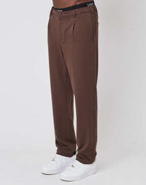 A person wearing LIVE FAST DIE YOUNG Regular Casual Pants with pleats, an elastic waist, a black LFDY waistband, and white sneakers stands against a plain white background.