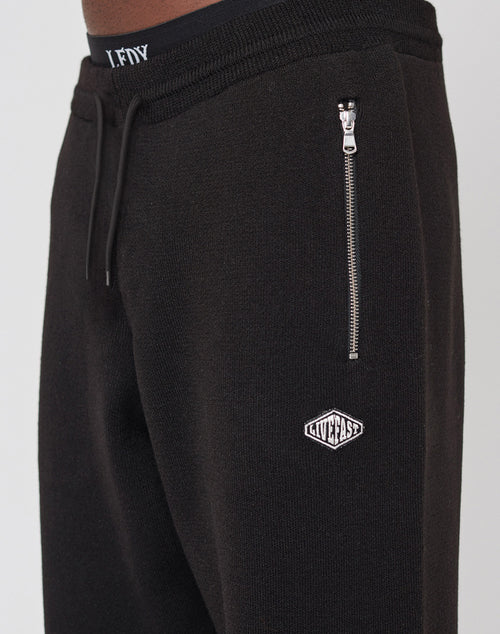 Close-up of black Knit Jogger by LIVE FAST DIE YOUNG, featuring an elastic waistband with LFDY branding, drawstring, vertical zippered pocket, and small white LUXEFAST logo patch.