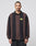 A man wears the LFDY® Polo Longsleeve by LIVE FAST DIE YOUNG, an oversized, 100% Baumwolle shirt with brown and black vertical stripes, Polokragen, and a yellow oval logo on the chest, standing against a light gray background.