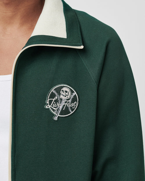 Someone wears a dark green LIVE FAST DIE YOUNG Track Suit Jacket with a skull and Live Fast embroidered patch on the chest, layered over a white shirt.